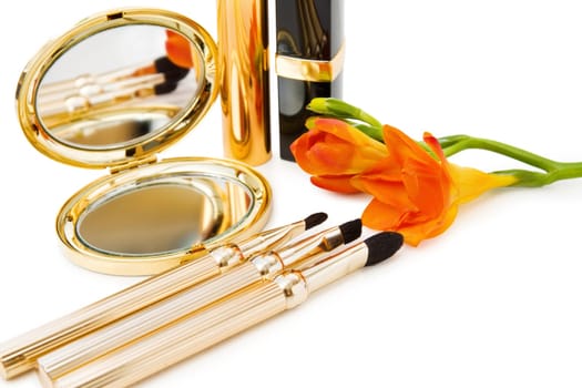 Spring makeups in golden and black. With mirror, set of brushes, lipstick, mascara and a freesia flower. Isolated over white.