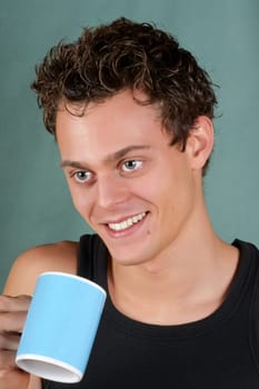 Smiling young caucasian man holding a light blue mug over a green background.