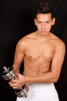 Shirtless young man training with a chrome dumbbell over a black background. Soft focus.