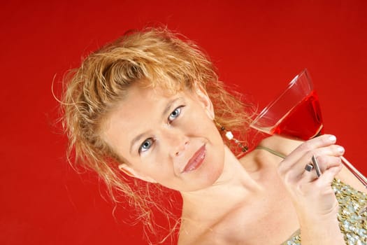Portrait of a beautiful blond woman with blue eyes, wearing a green sequins top, holding a red drink, over a red background. Selective focus.