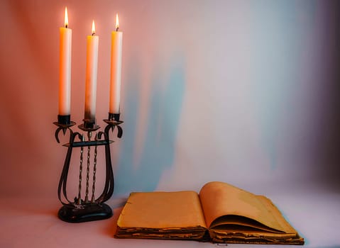 An open vintage book with yellowed pages and an antique candelabrum with burning candles, set against a soft warm light, creating a mysterious and cozy atmosphere
