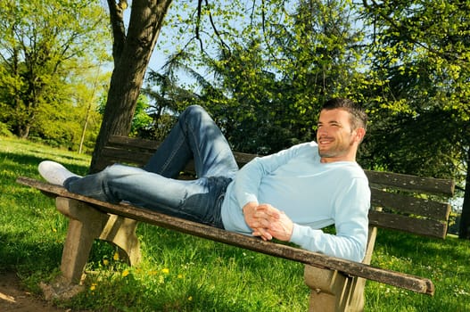 attractive man is relaxing on a bench in a natural environement