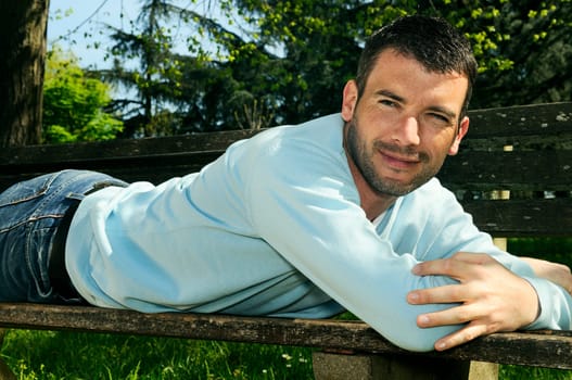 attractivz man is relaxing on a bench in a natural environement