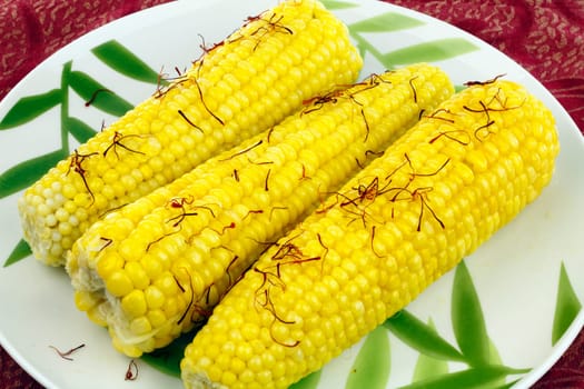 Three bright, buttered yellow vegetable ears topped with strands of red orange crocus stigmas.