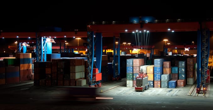 Busy Commercial Container port at night with cranes and cars moving containers