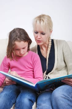Mother and daughter sitting in living room reading book