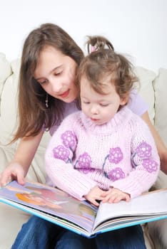 Sisters sitting in living room reading book