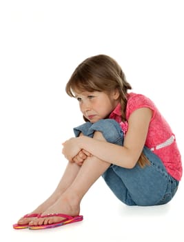 Young girl sitting, hugging knees, sad facial expression, on white.