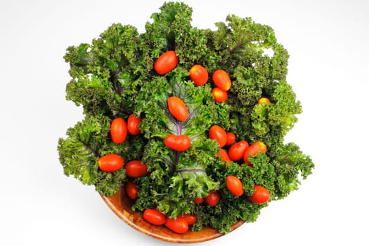 Small red cherry tomatoes on top of red kale in a wood bowl on white background.