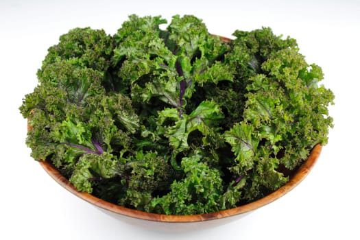 Wood bowl of red kale, green leaf with purple veins, on a white background.