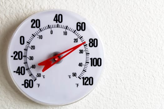 White round thermometer on an inside wall near 80 degrees Fahrenheit.
