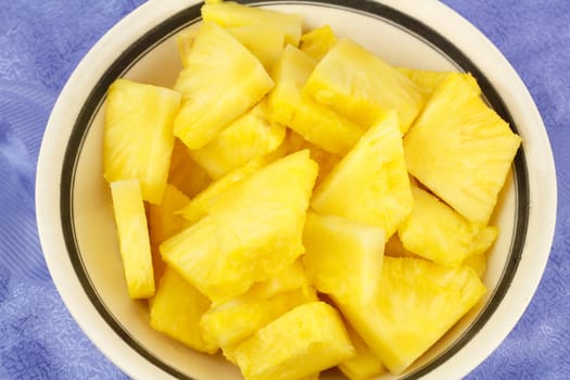 Tropical golden yellow fruit pieces in a white bowl with blue background.