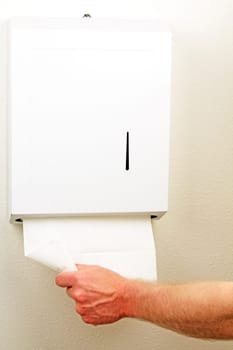 A hand is pulling down and out a white folded sheet of disposable paper to dry hands from a wall box.