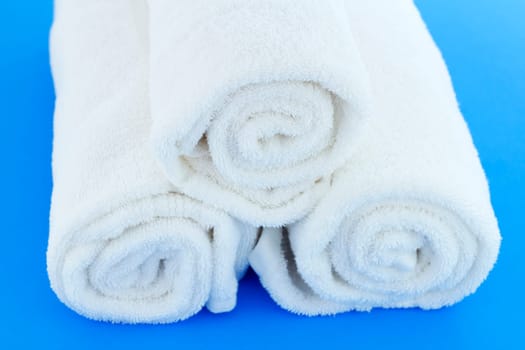 Three large white cotton bath cloths rolled up individually and piled together on a blue background.