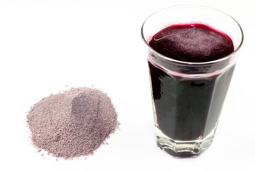 Violet purple dried and ground extract mix of berries and similar with a glass of the beverage made with water.