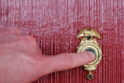 Finger of a man&#039 s hand ringing a gold and black door bell on a brick red house.