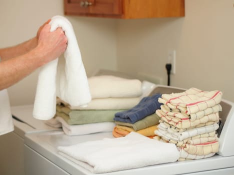 Arms and hands of a male folding towels onto a dryer and washer in a laundry room.