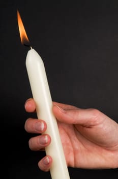 Woman&#039 s hand holding a candle, against black background.