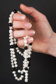 Woman&#039 s hand holding a necklace with black and white pearls against black background.