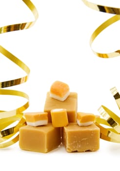 Celebrating food - caramel fudge and vanilla candy with golden ribbons. Isolated over white background.