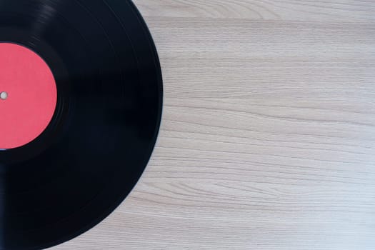 Black vinyl record with a red label on a wooden background, leaving empty space for text or design. Perfect for music, retro, and nostalgia-themed projects