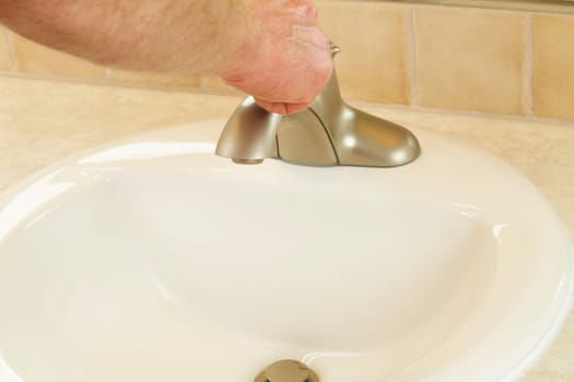 Close up of a person about to turn on the water in a modern bathroom sink.