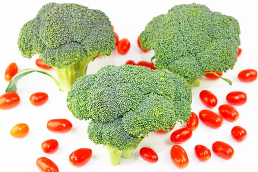 Three crowns of green vegetable standing upright with many small red fruit on white.