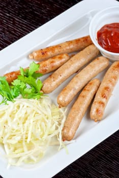 Grilled sausages with cabbage, greens and tomato sauce on white plate