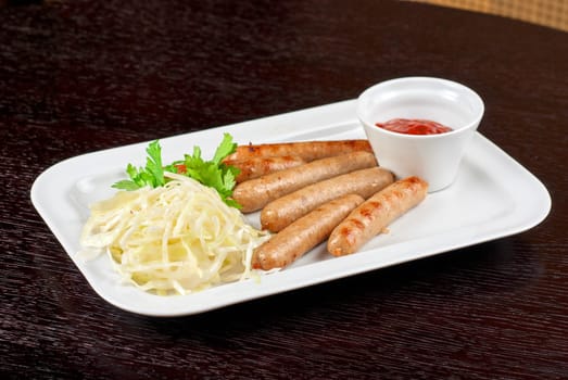 Grilled sausages with cabbage, greens and tomato sauce on white plate