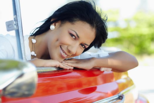 young adult brunette woman leaning on convertible red car and looking at camera. Horizontal shape, side view