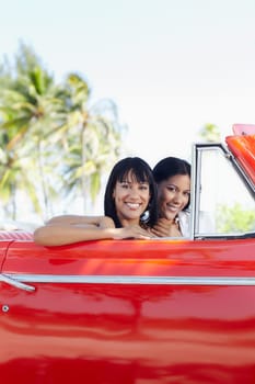 young adult brunette twin women driving convertible red car and looking at camera. Vertical shape, side view, copy space