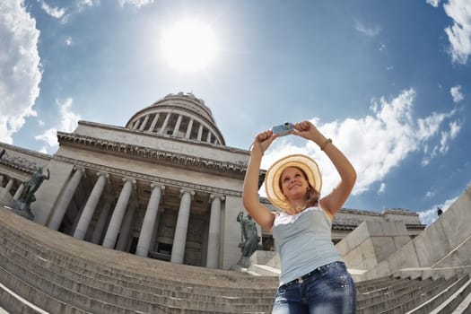 young adult blonde woman taking picture with digital camera in Havana, Cuba. Horizontal shape, waist up, low angle