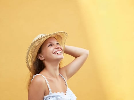 young adult blonde woman in straw hat laughing against yellow wall. Horizontal shape, side view, copy space