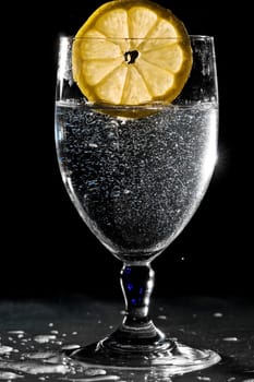 Slice of lemon drops into a glass of water and splashes