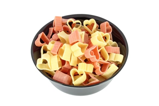Raw colored pasta in form of heart in black bowl isolated on white background