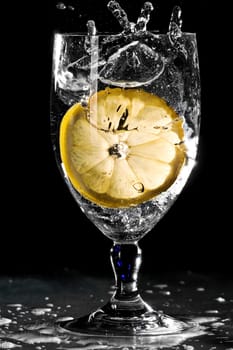 Slice of lemon drops into a glass of water and splashes