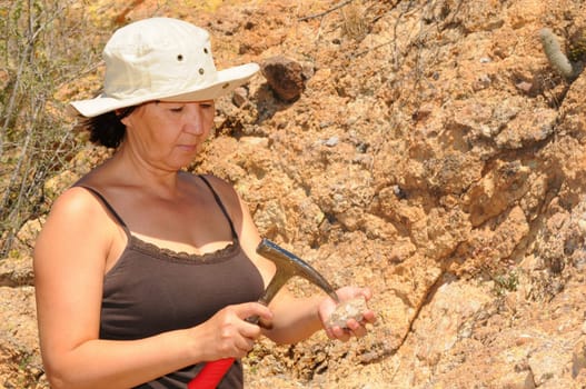 Senior woman geologist tap a rock formation with a hammer