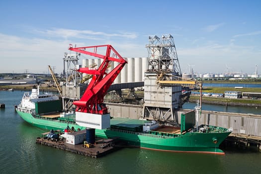 Grain elevator in harbour with terminal and cranes for transhipment and a ship getting loaded