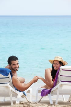 husband and wife relaxing on sunbeds on the beach and smiling at camera. Vertical shape, rear view, copy space