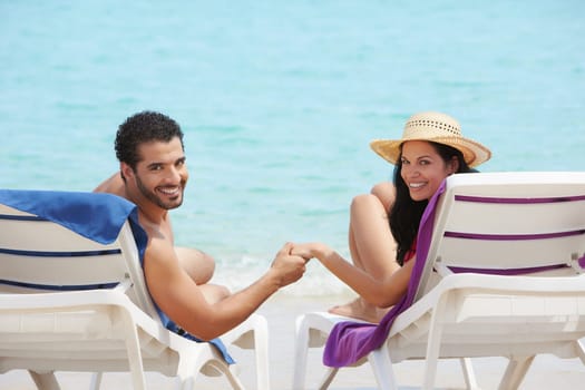 husband and wife relaxing on sunbeds on the beach and smiling at camera. Horizontal shape, rear view, copy space