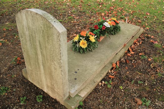Tomb covered with colored flowers with autumn colored red leaves in a cemetery