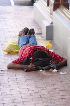 A poor beggar lying on the side of a street in the dirt in Cape Town