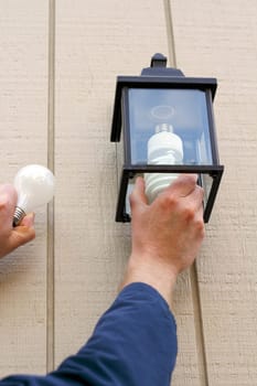 Man carefully replacing an old incandescent lightbulb with a new CFL light in an outdoor fixture to save money when the lamp is on.