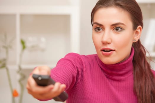 surprised young woman with remote control watching television