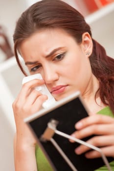 Crying woman with handkerchief on sofa looking at framed picture