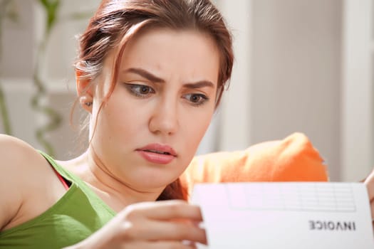 shocked young woman holding bill at home