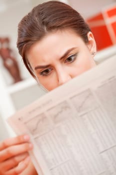 woman reading shocked news in newspaper at home