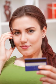 young woman on phone holding credit card at home