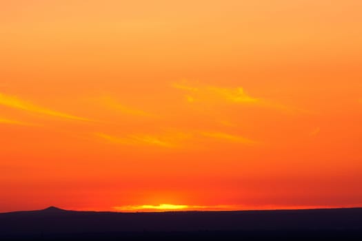 Beautiful orange sunset with the silhouette of a small mountain