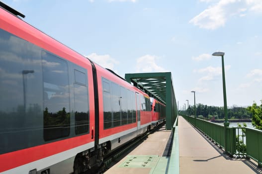 Red passenger train goes through the railway bridge. (Northern Railway Bridge over river Danube in Budapest, Hungary)